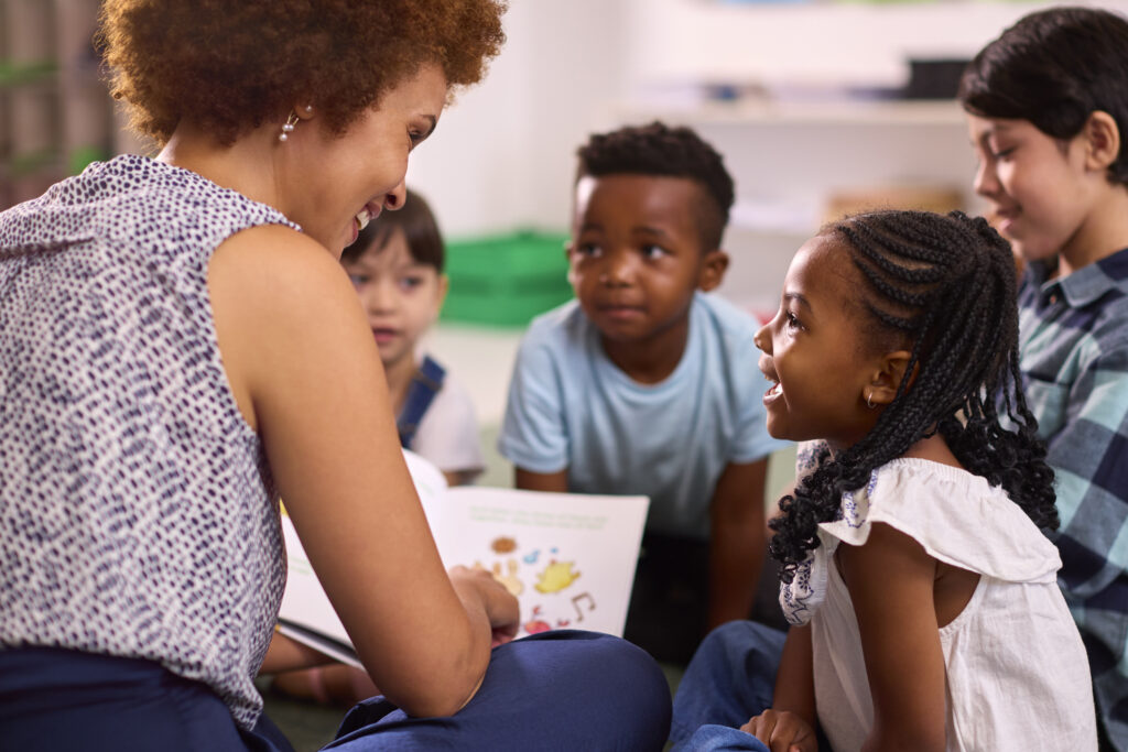 Teacher engaging with a small group of young children during story time in a classroom, representing types of child education franchises.